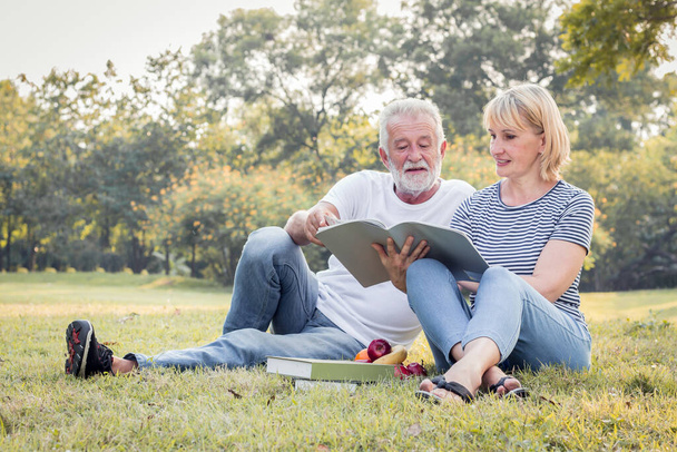Elderly couple reading together in the park in the morning. Concept of couples elderly good healthy and strong. Grandfather and grandmother read a book sitting on the grass. - Foto, imagen
