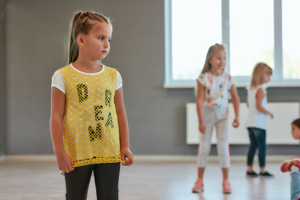 Portré egy aranyos kislányról, aki félrenéz, miközben koreográfia órán van. A tánciskolában álló gyerekek csoportja - Fotó, kép