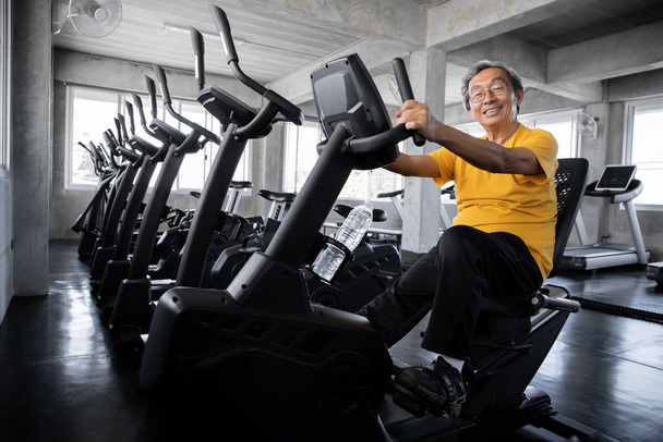 Starsi mężczyźni ćwiczą kręcąc rowerem na siłowni. Pojęcie zdrowych osób starszych z wysiłkiem fizycznym. Azji Dojrzałe mężczyźni grać maszyny do ćwiczeń w siłowni - Zdjęcie, obraz
