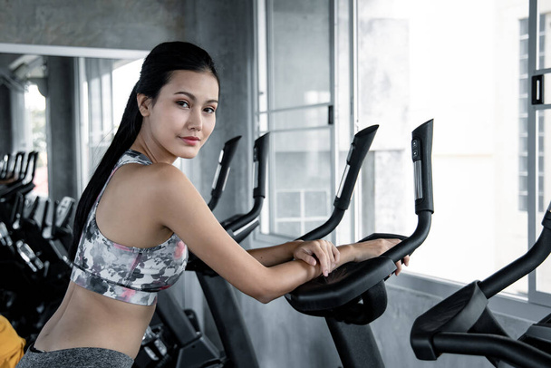 Las mujeres jóvenes asiáticas están haciendo ejercicio con el cardio en la máquina de ejercicios en el gimnasio con sonrisa. Concepto de atención de salud con ejercicio en el gimnasio. Hermosa chica jugando fitness en el gimnasio
. - Foto, Imagen