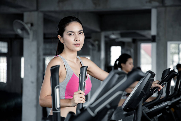 Giovani donne asiatiche si allenano con il cardio sulla macchina da ginnastica in palestra con il sorriso. Concetto di assistenza sanitaria con esercizio in palestra. Bella ragazza che gioca a fitness in palestra
. - Foto, immagini