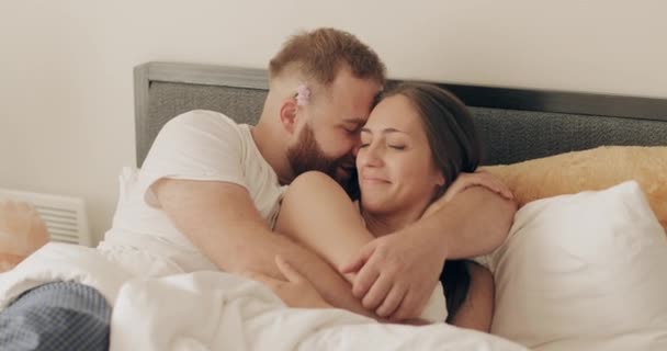 Happy man and woman having good time and playing childish in bed. Smiling husband whispering in ear his beautiful wife and enjoing intimate moments in morning. Concept of good relationship. - Filmagem, Vídeo