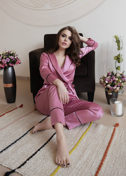 a beautiful gentle girl in silk satin pajamas at home, she is cozy and comfortable, she is resting and working at home. - Foto, Imagem