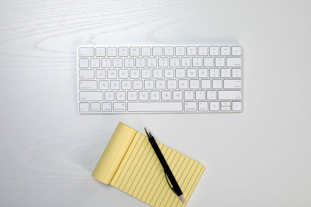 draadloos toetsenbord en geel notitieblok op tafel - Foto, afbeelding