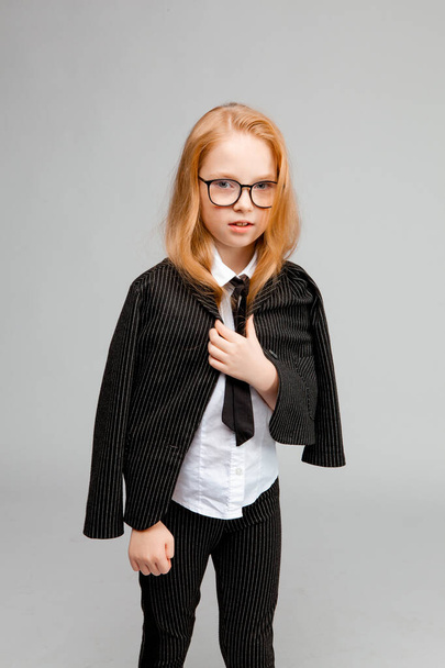 Cute red-haired girl in a business suit and tie looks seriously. - Photo, Image