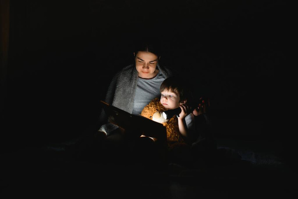 Family Mom and little son reading a book with a flashlight under the blanket. - Fotografie, Obrázek