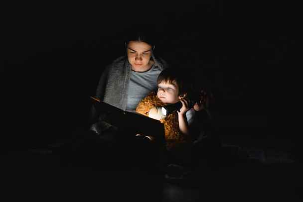 Šťastná rodina. Čas na historky. Potěšený šťastný roztomilý maminka a syn těší knihu před spaním a pomocí baterky. - Fotografie, Obrázek