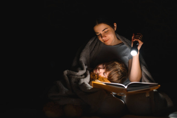 Happy family. Time for stories. Delighted happy cute mother and son enjoying a book before sleeping and using a flashlight. - Фото, зображення