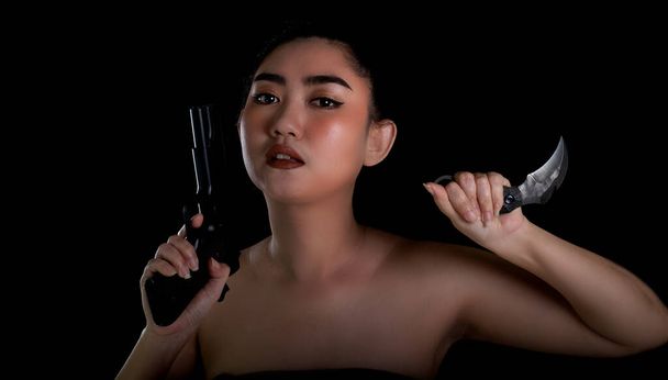 Portrait beautiful Asia woman one hand holding a gun and karambit knife at the black background, Young sexy girl long hair with a handgun, Pretty women stand with a pistol, look at camera - Foto, Bild