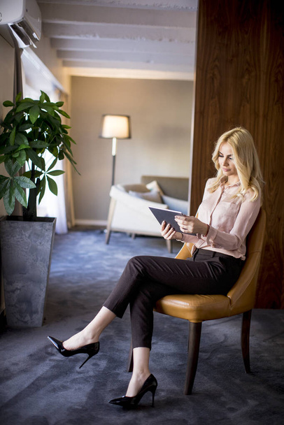 Krásná mladá běloška blondýnka sedící u okna v obývacím pokoji a používající digitální tablet - Fotografie, Obrázek