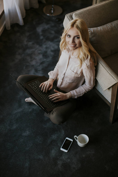 Genç ve güzel bir kadın dizüstü bilgisayarla odada oturuyor. - Fotoğraf, Görsel