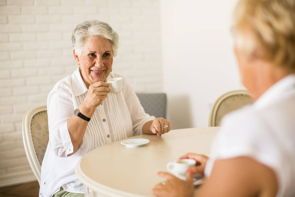 Idős anya és idős lánya beszélgetnek és kávét isznak a szobában. - Fotó, kép