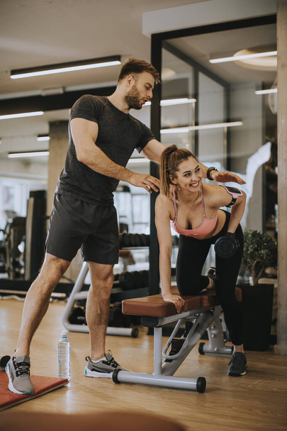 Mulher atraente e um personal trainer com treinamento de peso dumbbell no ginásio
 - Foto, Imagem