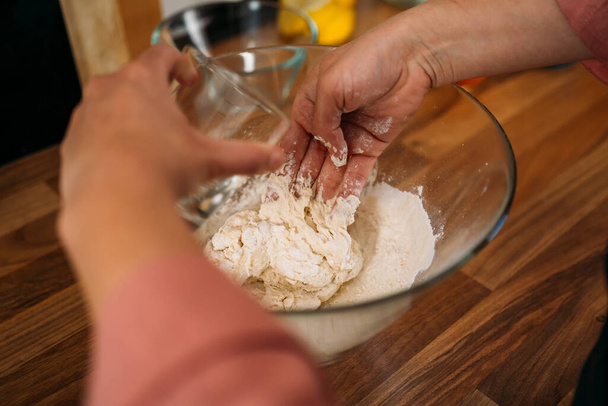 Close up of a Woman pouring a some water into a bowl with flour and kneading to make a dough for pizza in her home kitchen - Foto, imagen