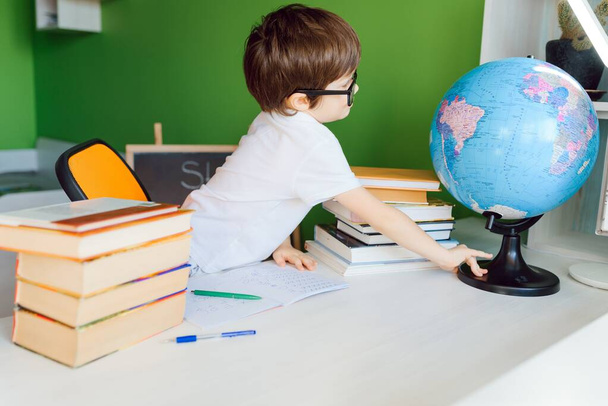 Fünfjähriges Kind liest zu Hause ein Buch. Junge lernt am Tisch auf grünem Hintergrund - Foto, Bild