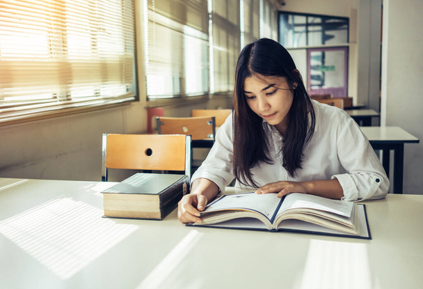 Jovem mulher asiática lendo livro na biblioteca
 - Foto, Imagem
