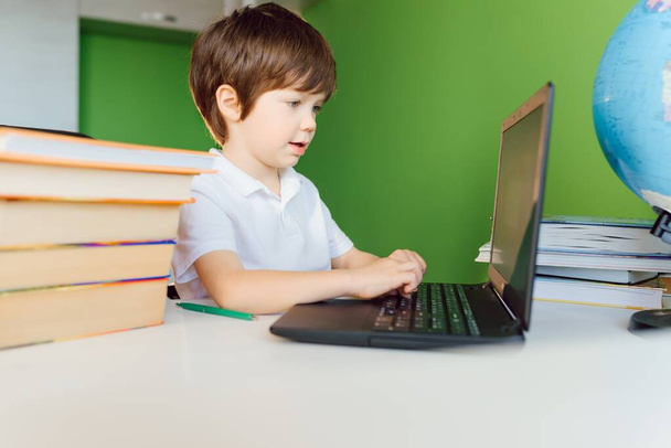 Хлопчик вчиться вдома з блокнотом і робить домашнє завдання в школі. Дистанційне навчання онлайн
. - Фото, зображення