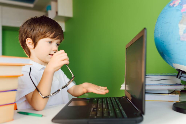 Boy studying at home with notebook and doing school homework. Distance learning online education. - Zdjęcie, obraz