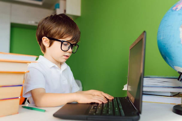 Boy studying at home with notebook and doing school homework. Distance learning online education. - Foto, afbeelding