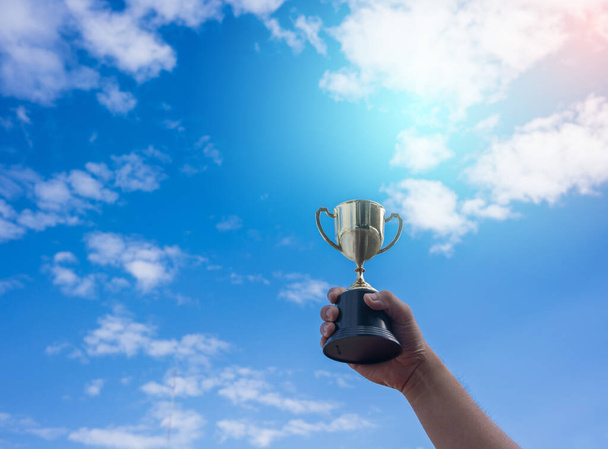 Conceito de vitória, Homem segurando uma taça de troféu de ouro é vencedor em uma competição com fundo azul céu
. - Foto, Imagem