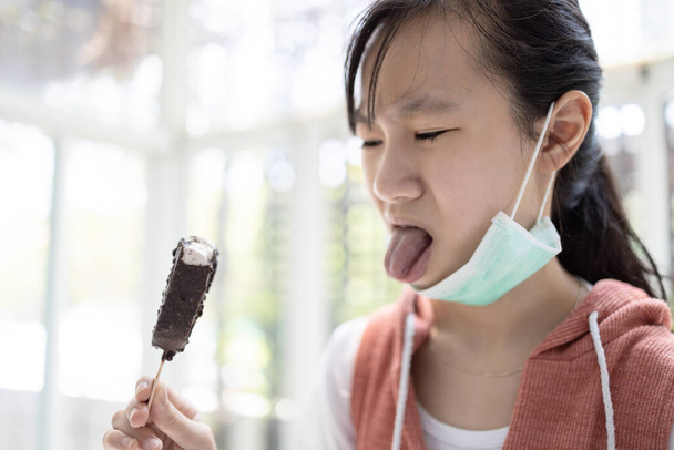 Menina asiática comendo sorvete, tem senso de gosto problemas com o receptor de sabor, sem apetite, anorexia, nojo com a língua para fora da boca, mau gosto, não extrair qualquer sabor, mulher triste entediado com alimentos
 - Foto, Imagem