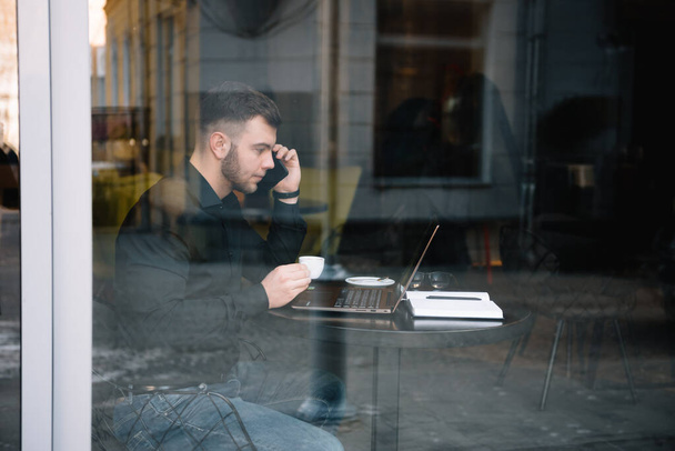 Молодий бізнесмен розмовляє на мобільному телефоні під час роботи на ноутбуці в кафе
 - Фото, зображення