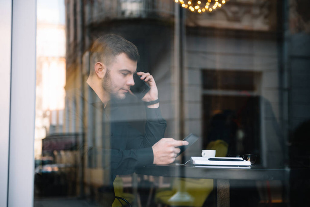 Joven hombre de negocios hablando en el teléfono móvil mientras trabaja en el ordenador portátil en la cafetería
 - Foto, imagen