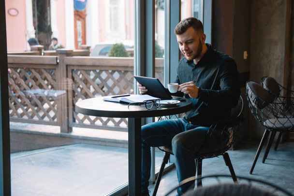 Handsome businessman using a digital tablet and drinking coffee while sitting in cafe in the city center - Фото, зображення