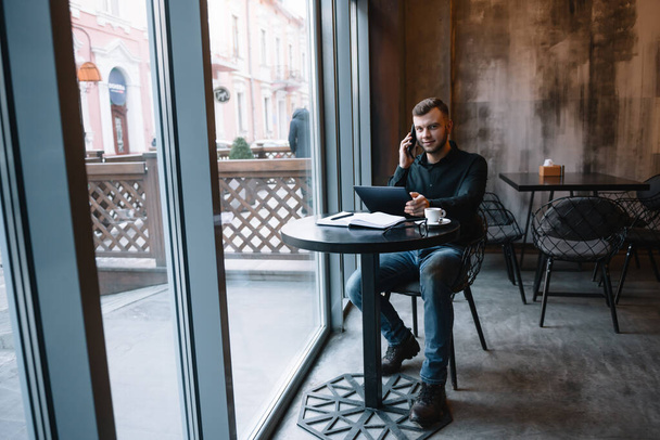Young businessman talking on mobile phone while working on tablet in cafe - Photo, image