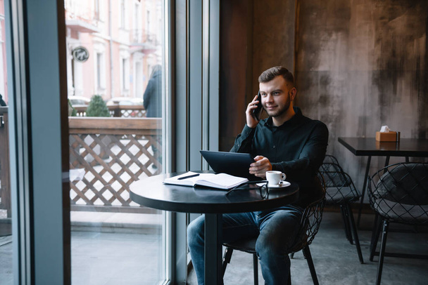 Young businessman talking on mobile phone while working on tablet in cafe - Фото, зображення
