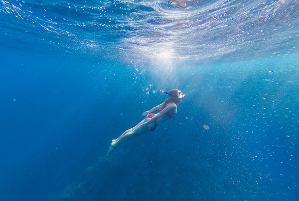 Chica con una máscara y un snorkel se sumerge en el mar con corales y peces
 - Foto, Imagen