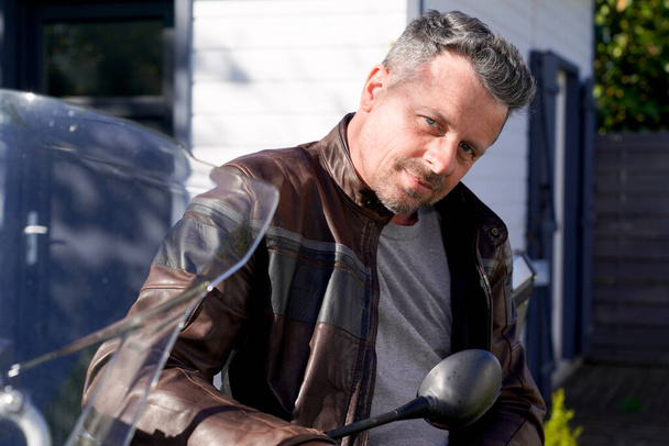 przystojny broda człowiek w brązowy motocykl moda kurtka siedzieć na motocykl zewnątrz - Zdjęcie, obraz