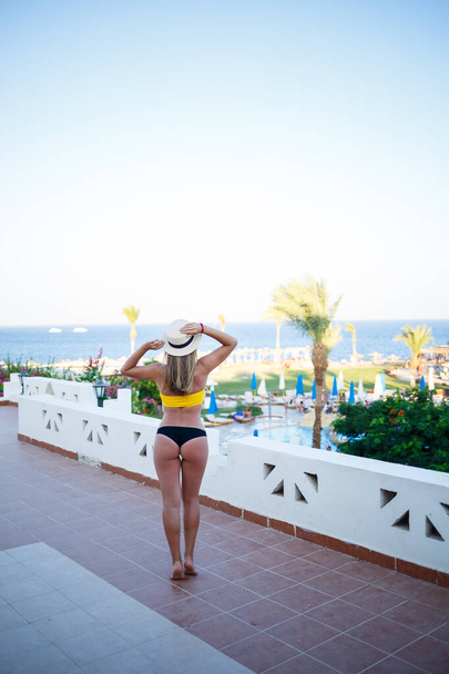 Hermosa chica con el pelo rubio y en un traje de baño amarillo se relaja en una terraza contra el mar
 - Foto, imagen