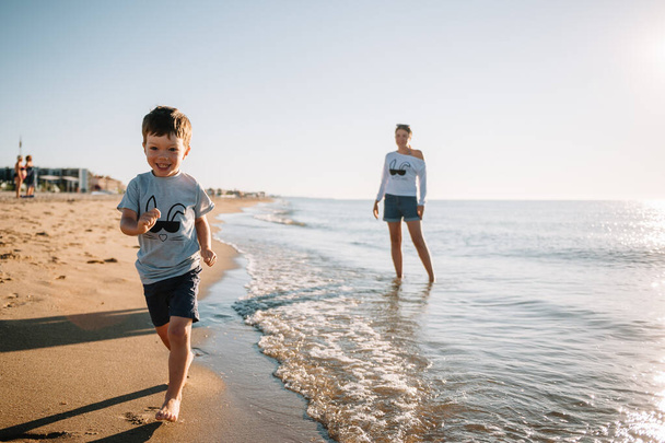 Mutter und Sohn spielen am Strand bei Sonnenuntergang. Konzept der freundlichen Familie. - Foto, Bild