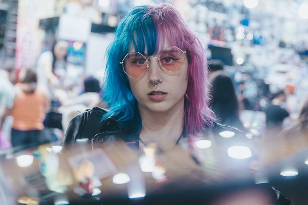 A beautiful young female with sunglasses and a leather jacket in front of an illuminated amusement park at night - 写真・画像