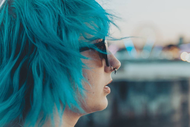 A portrait of a young female with blue and pink hair wearing sunglasses with a blurred background - Photo, Image
