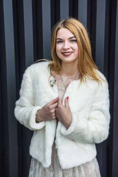 Fashion. Elegant woman in beige dress wearing in white fur coat. Beautiful girl model in luxurious clothes posing on abstract background. Outdoor closeup portrait. - Foto, immagini