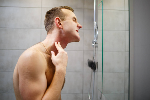 Muž si holí obličej elektrickou holicí stroječkou před zrcadlem. Dráždivost pro kůži. Koupací procedura - Fotografie, Obrázek