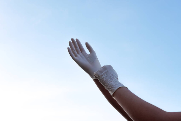 De armen van een persoon dragen corona virus beschermende handschoenen met de lucht op de achtergrond - Foto, afbeelding