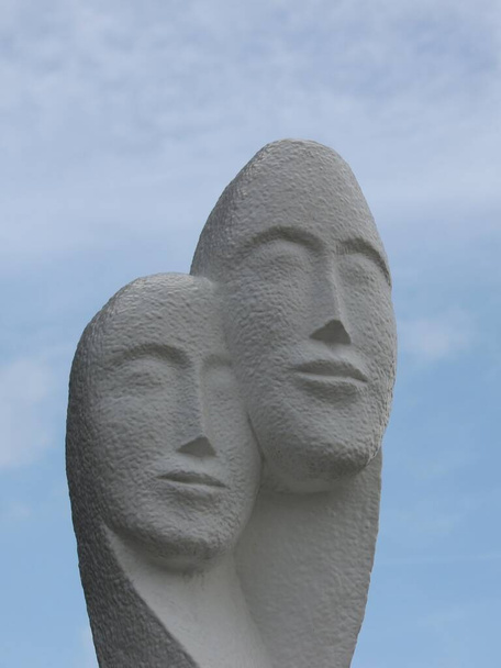 Сучасна бетонна статуя чоловічого і жіночого обличчя близько один до одного на фоні блакитного неба
 - Фото, зображення