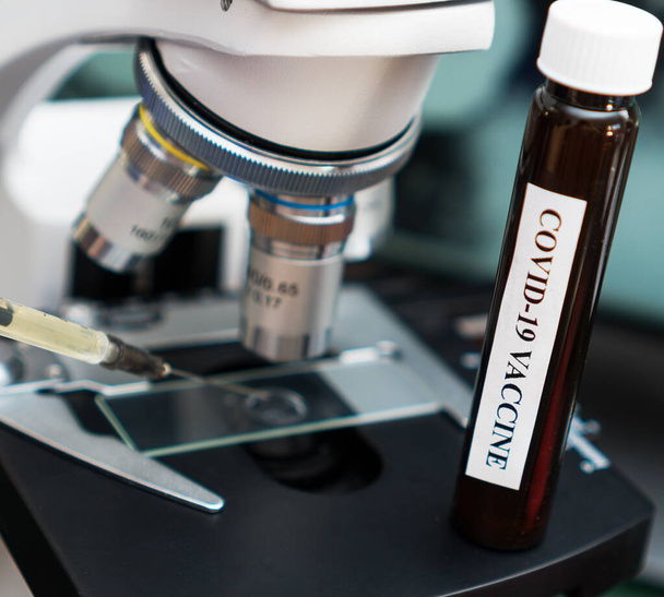 Εμβόλιο του Coronavirus που στέκεται κοντά στο μικροσκόπιο στο εργαστήριο. - Φωτογραφία, εικόνα