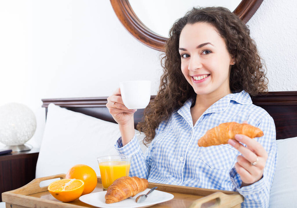 Portrait of curly haired woman with tasty breakfast in be - Photo, Image