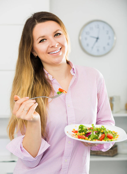 Cheerfull young woman eating tasty green salad at hom - 写真・画像