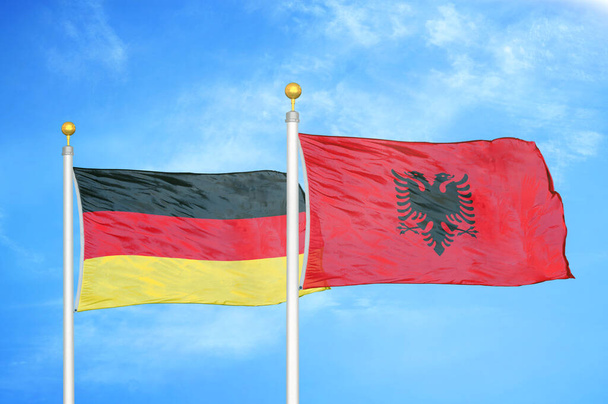 Německo a Albánie dvě vlajky na vlajkových stožárech a modrá oblačná obloha pozadí - Fotografie, Obrázek