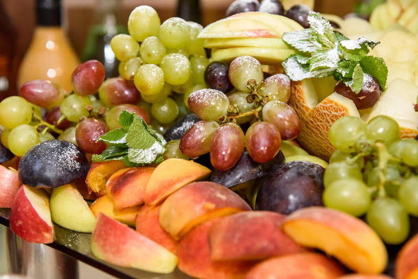 Νόστιμα και πολύχρωμα φρούτα με φύλλα δυόσμου στο πιάτο από κοντά - Φωτογραφία, εικόνα