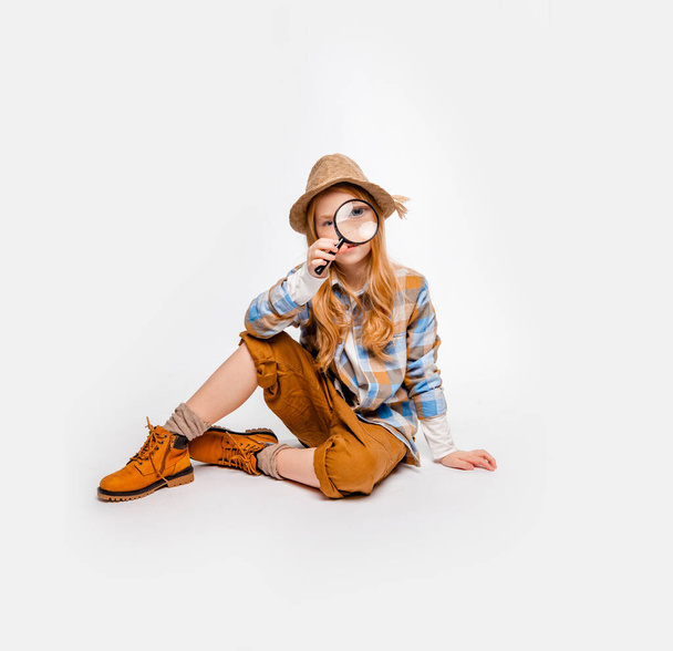 menina de cabelos longos em roupas de viajante senta-se no chão e olha através de uma lupa
 - Foto, Imagem