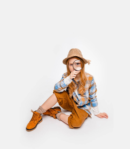 menina de cabelos longos em roupas de viajante senta-se no chão e olha através de uma lupa
 - Foto, Imagem