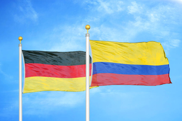 Γερμανία και Κολομβία δύο σημαίες σε κοντάρια σημαίας και φόντο μπλε συννεφιασμένο ουρανό - Φωτογραφία, εικόνα