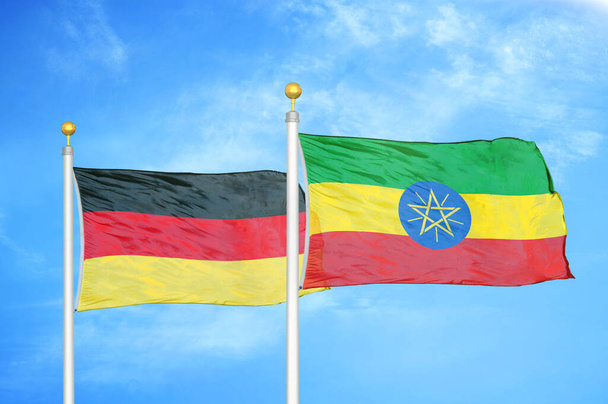 Γερμανία και Αιθιοπία δύο σημαίες σε κοντάρια σημαίας και φόντο μπλε συννεφιασμένο ουρανό - Φωτογραφία, εικόνα