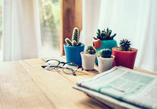 Oficina de trabajo con periódico, vasos y cactus sobre mesa de madera
. - Foto, Imagen